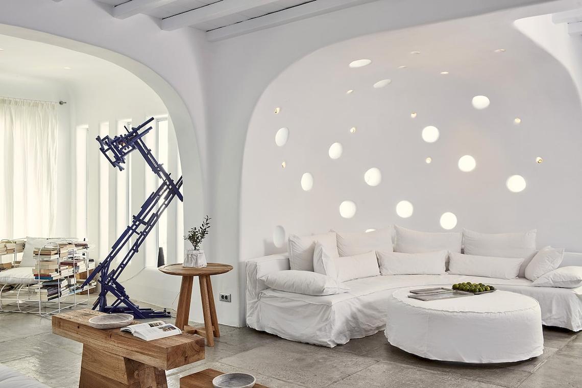 Innenbereich des Mykonos Ammos Hotels mit weißer Wand, Sofa, Tisch und Lampe.