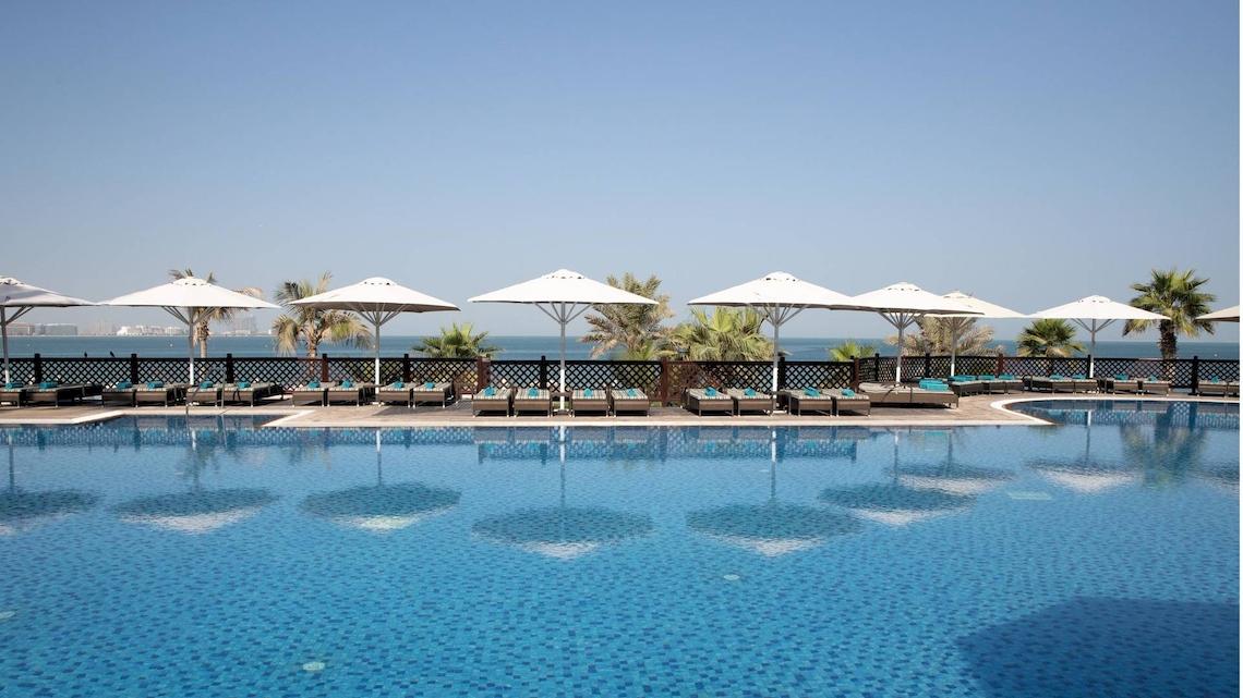 Außenpoolbereich des Jumeirah Mina A'Salam Hotels mit Sonnenliegen und Sonnenschirmen am Meer