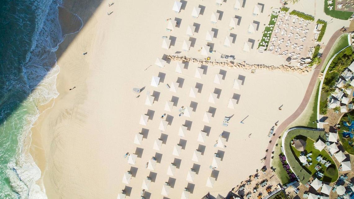Luftaufnahme des Jumeirah Mina A'Salam Strandes mit vielen weißen Sonnenschirmen und Gästen.