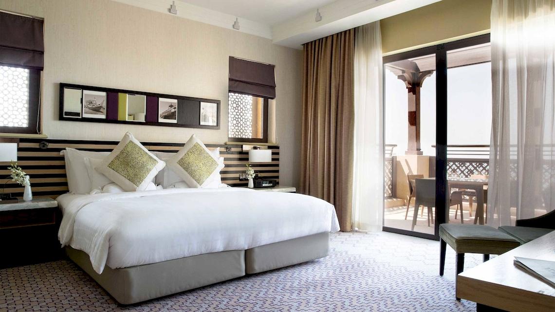Hotelzimmer im Jumeirah Mina A'Salam mit großem Bett, Balkon und Gartenblick.