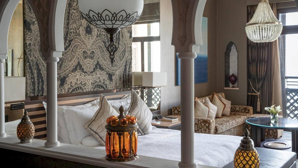 Luxuriöses Hotelzimmer im Jumeirah Mina A'Salam mit üppigen Kissen, eleganten Kronleuchtern und einem Blick auf das Meer.