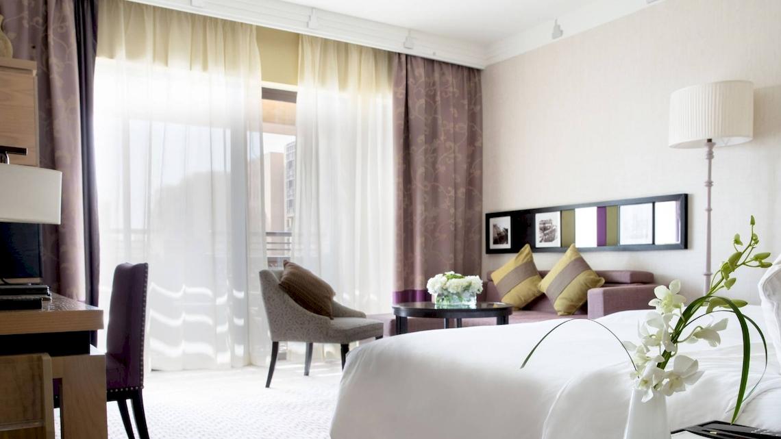 Ein elegantes Hotelzimmer im Jumeirah Mina A'Salam mit einem großen Bett, einem Schreibtisch und einem Wohnzimmerbereich.