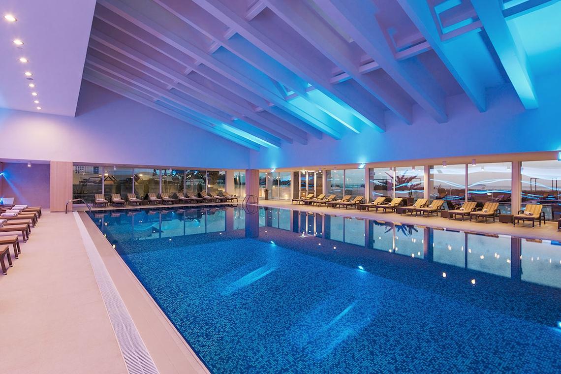 Innenpool des Hotels Dubrovnik President Valamar Collection mit Loungestühlen und blauer Beleuchtung.