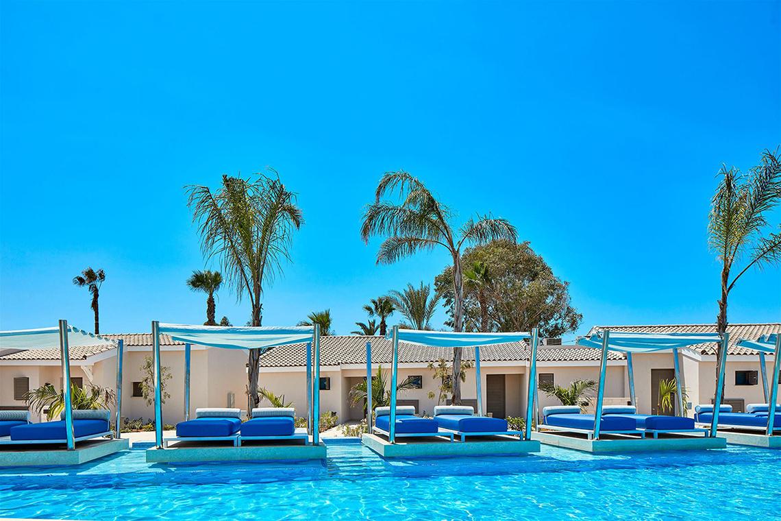 Pool-Lounge-Bereich im Mare Ayia Napa Hotel mit blauen Sonnenliegen unter weißen Sonnendächern.