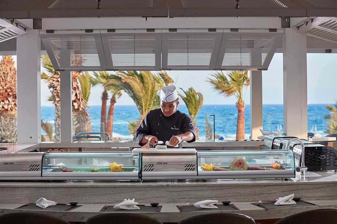 Ein Koch bereitet Sushi in einer Glasfalle im Mare Ayia Napa Hotel zu, mit Blick auf das Meer.