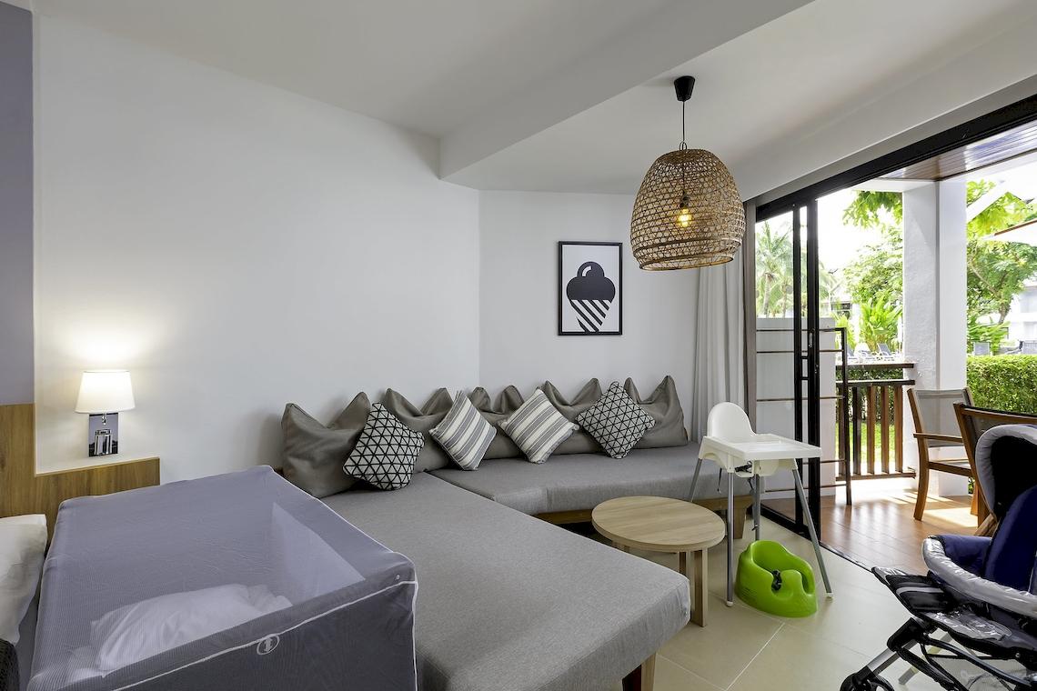 Hotelzimmer im Sunwing Kamala Beach mit L-förmigem Sofa, Nachttisch und Babystuhl.