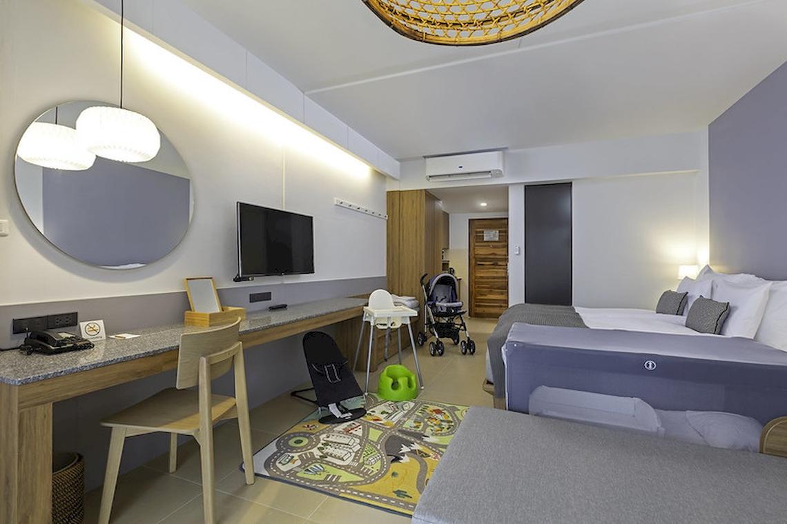 Innenansicht eines Hotelzimmers im Sunwing Kamala Beach mit Schreibtisch, Stuhl, Fernseher, Spiegel, Babystuhl und Kinderbett.