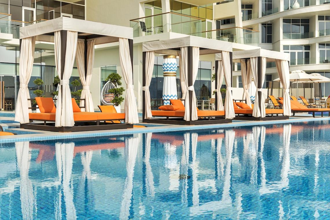 Außenpool mit orangefarbenen Loungestühlen im Royal Central Hotel The Palm