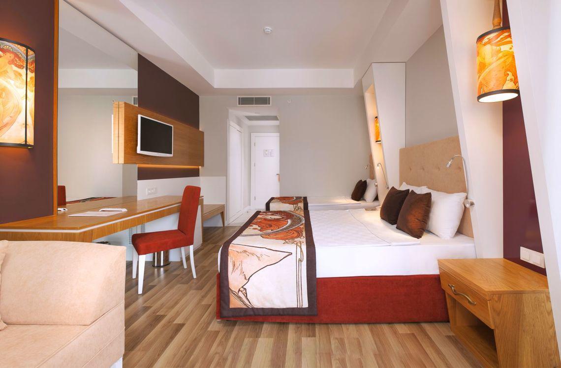 Innenansicht eines Hotelzimmers im Side Orange Palace mit zwei Betten, Schreibtisch und Möbeln.