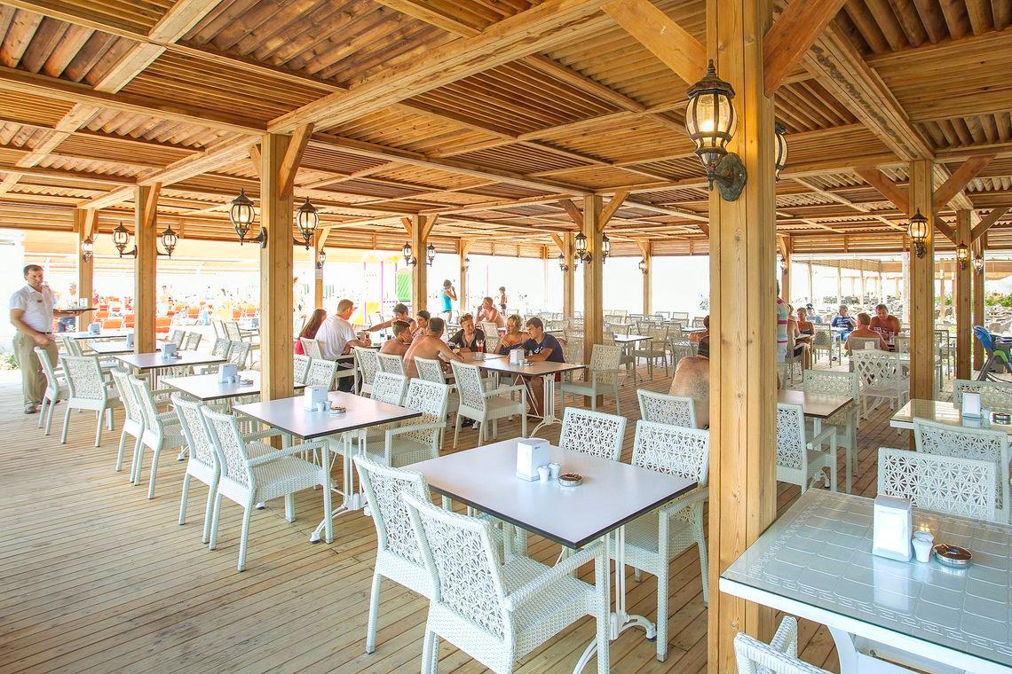 Terrasse des Side Orange Palace Hotels mit Gästen an Tischen unter Holzsäulen.