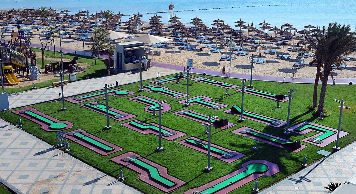 Luftaufnahme des Minigolfplatzes im Pickalbatros White Beach Resort mit Grün, roten Wegen und Strand im Hintergrund.