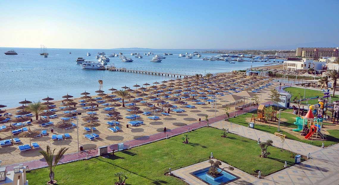 Luftaufnahme des Pickalbatros White Beach Resorts mit vielen Liegen und einem Spielplatz am Strand.