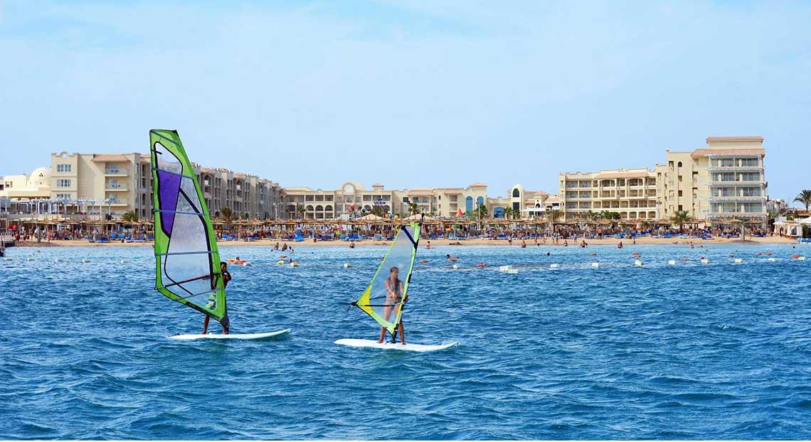 Zwei Personen windsurfen vor dem Pickalbatros White Beach Resort Hotel am Strand.