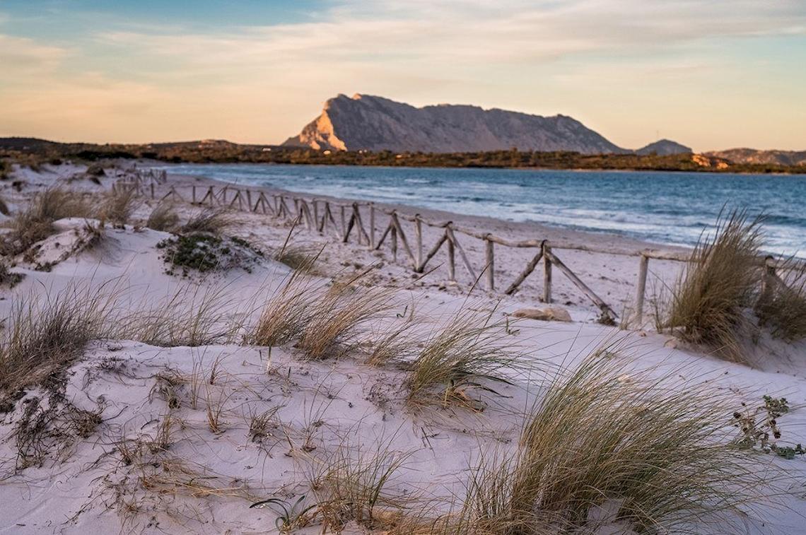 Hotel Ollastu Resort Strand bei Sonnenuntergang mit Dünen und Felsen im Hintergrund