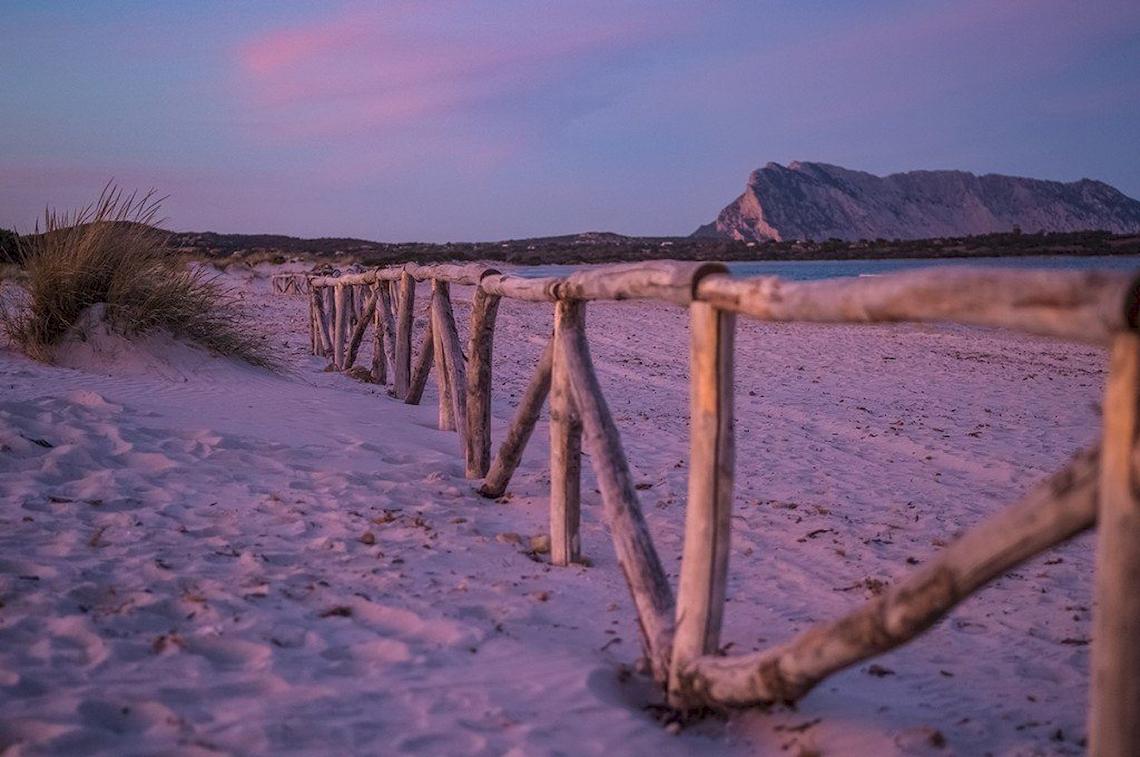 Strand mit Holzzaun und Berg im Hintergrund bei Sonnenuntergang