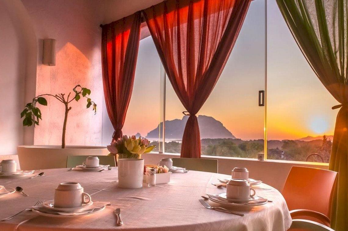 Speisezimmer im Hotel Ollastu Resort mit Tisch, Blick auf einen Berg und den Sonnenuntergang.