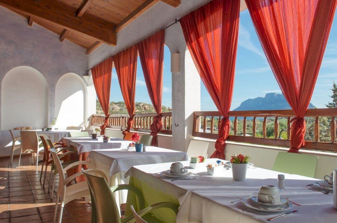 Terrasse des Hotel Ollastu Resort mit roten Vorhängen und Blick auf die Berge