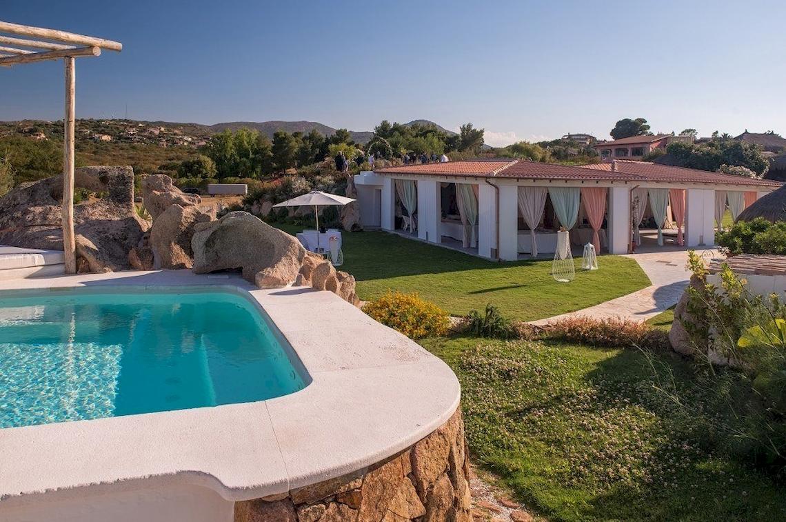 Außenbereich des Hotel Ollastu Resort mit Swimmingpool, Sonnenschirm und Loungemöbeln.