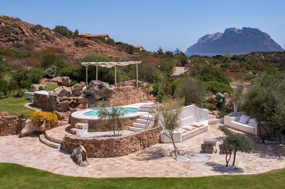 Außenbereich des Hotel Ollastu Resort mit Swimmingpool, Steinmauer und Garten