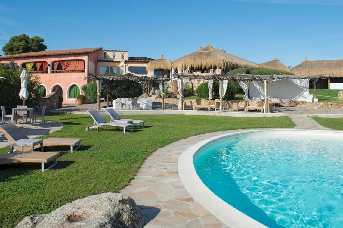Außenbereich des Hotel Ollastu Resort mit Pool, Liegestühlen und Sonnenschirmen.