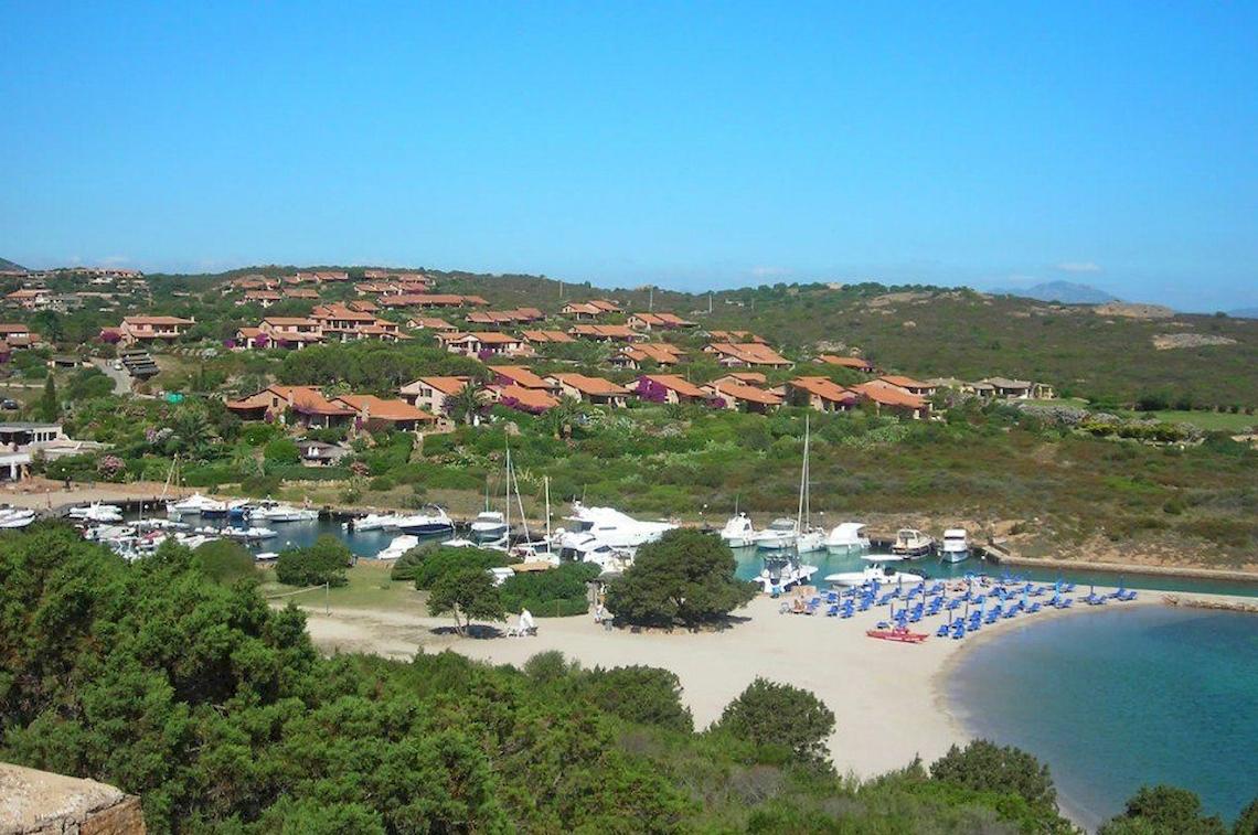 Luftaufnahme des Hotel Ollastu Resorts mit vielen Häusern, Booten im Hafen und Strandliegen