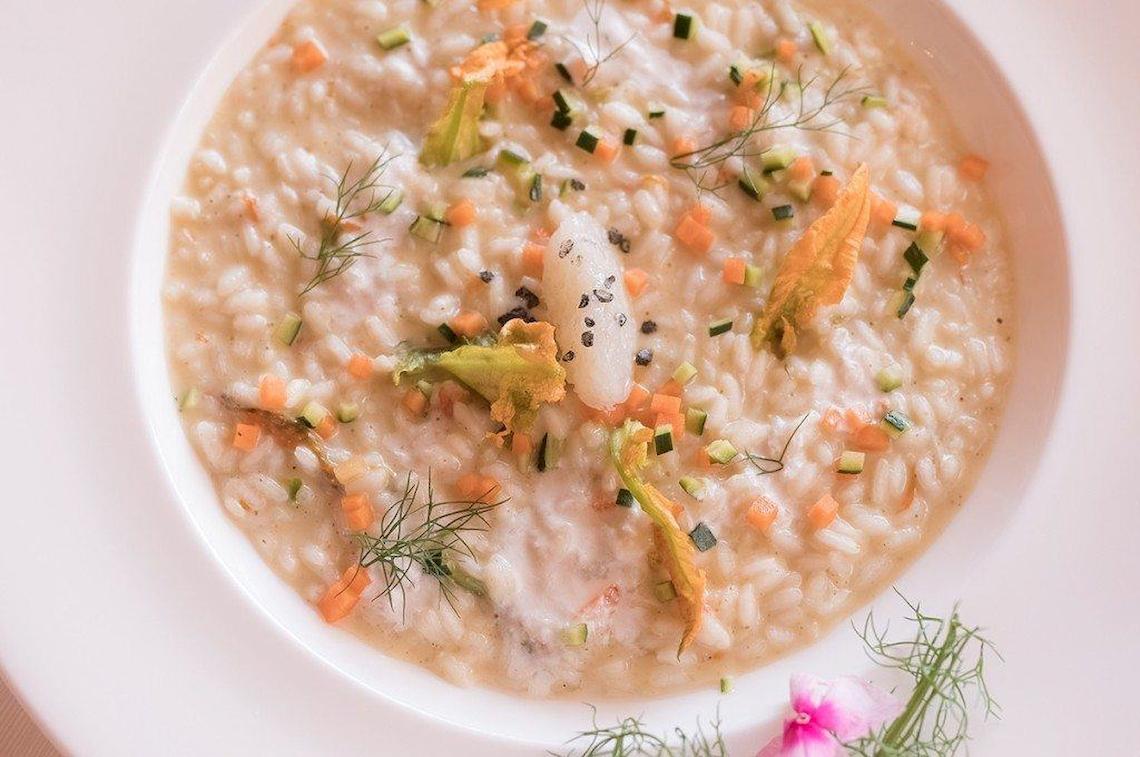 Eine Schüssel mit Risotto gefüllt mit Gemüse und Fisch, dekoriert mit Dill und Karotten.