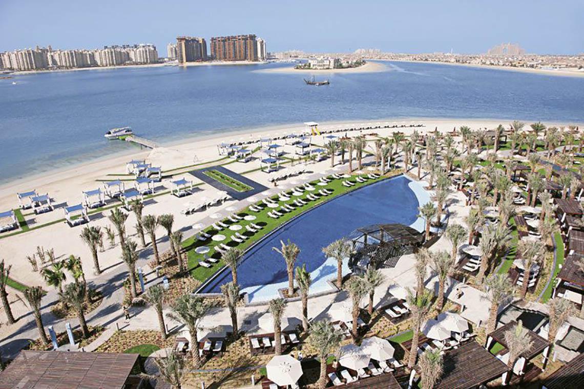 Luftaufnahme des Rixos The Palm Hotel & Suites mit Pool, Liegestühlen und Palmen