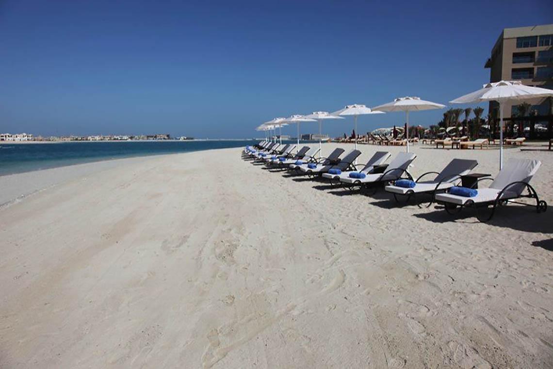 Strand mit Sonnenliegen und Sonnenschirmen im Rixos The Palm Hotel & Suites