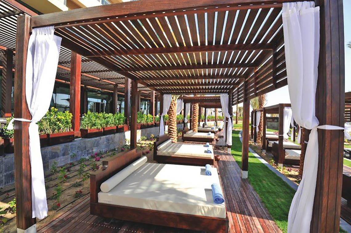 Lounge-Bereich mit Betten unter Holzpavillons im Rixos The Palm Hotel & Suites