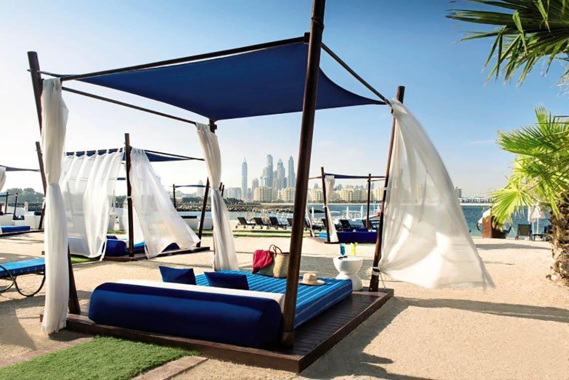 Strandbetten mit blauen Baldachinen und weißen Vorhängen im Rixos The Palm Hotel & Suites in Dubai.