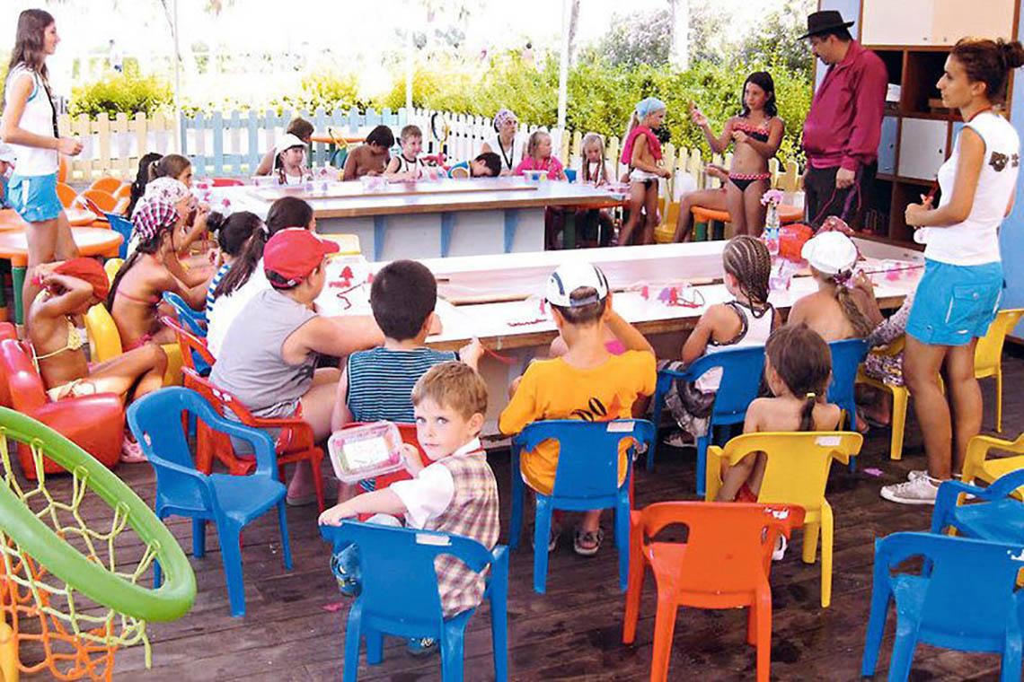 Kinder sitzen bei einem Bastelkurs im Freien im Rixos The Palm Hotel & Suites.