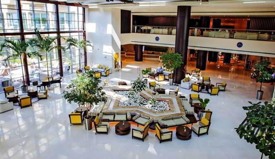Lobby des Rixos The Palm Hotel & Suites mit zentralem Brunnen, Sitzbereichen und Pflanzen.