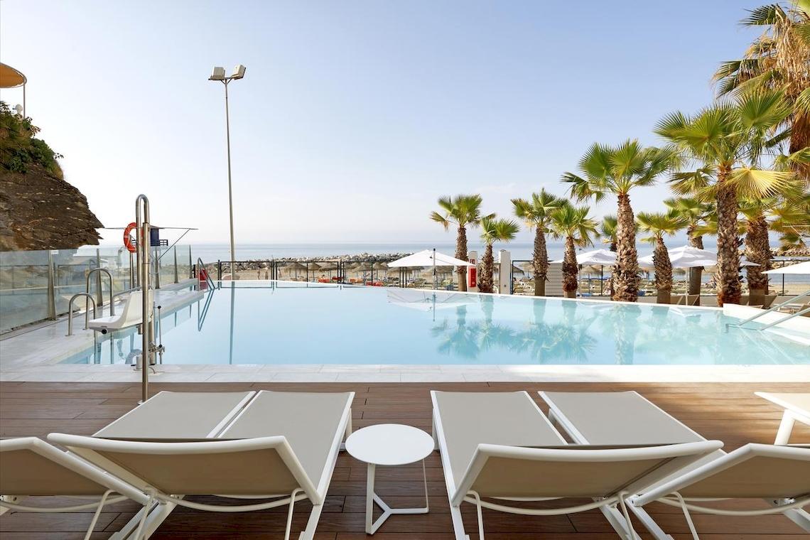 Pool-Lounge-Bereich im Playabonita Hotel mit weißen Liegen und einem kleinen Tisch.