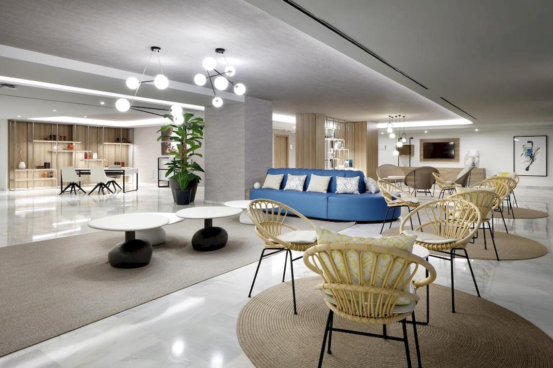 Lobby des Playabonita Hotels mit blauem Sofa, weißen Tischen und Rattanstühlen.