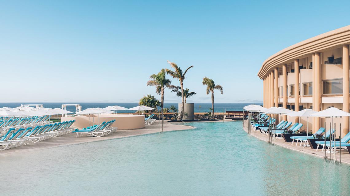 Außenpoolbereich des Iberostar Selection Fuerteventura Palace Hotels mit Lounge-Stühlen und Sonnenschirmen.