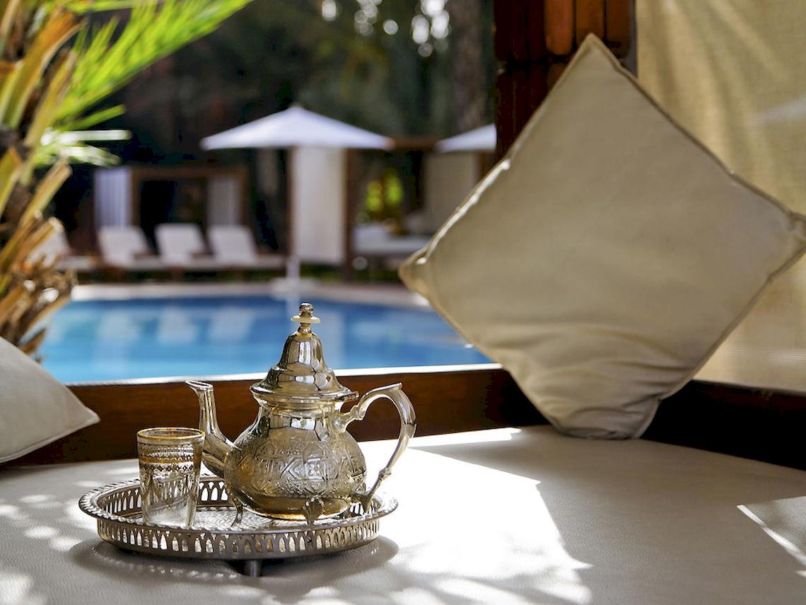 Lounge-Bereich im Sofitel Marrakech mit Blick auf den Pool, silberne Teekanne auf einer Tablett und ein Glas.