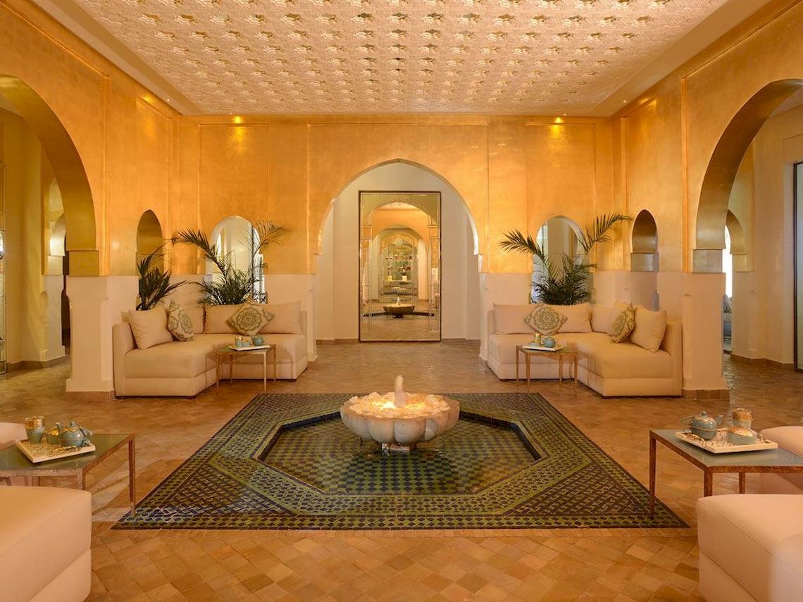 Innenansicht des Sofitel Marrakech Lounge & Spa mit gemusterten Teppichen, Sofas und einer zentralen Wasserfontäne.