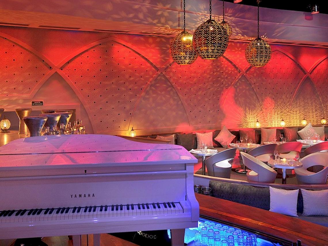 Innenbereich des Sofitel Marrakech Lounge & Spa mit einem weißen Klavier und roten Beleuchtung.