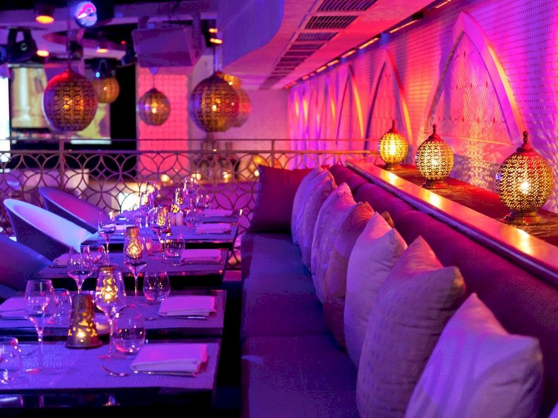 Innenbereich des Sofitel Marrakech Lounge mit blauer Beleuchtung, Sitzbänken und Tisch mit Gläsern und Servietten.
