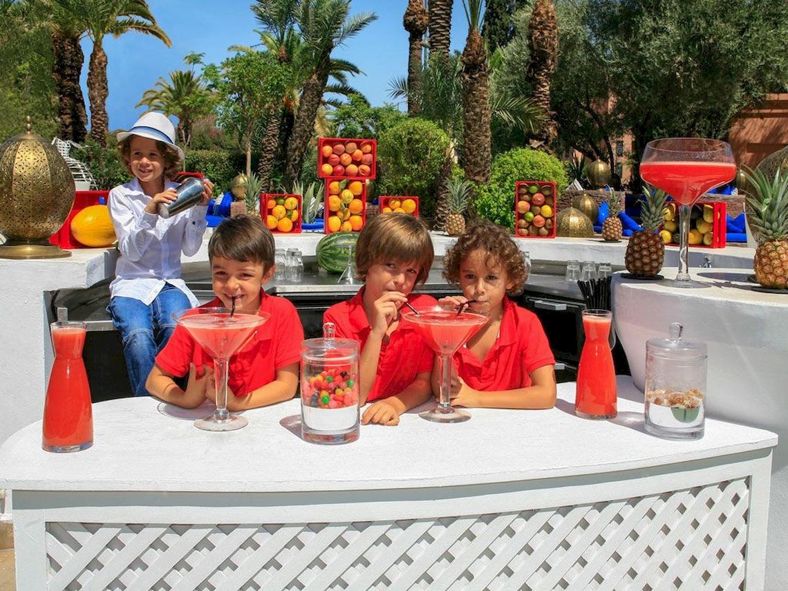 Kinder hinter einem Bartresen im Sofitel Marrakech Lounge & Spa mit selbstgemachten Getränken und Früchten im Hintergrund.
