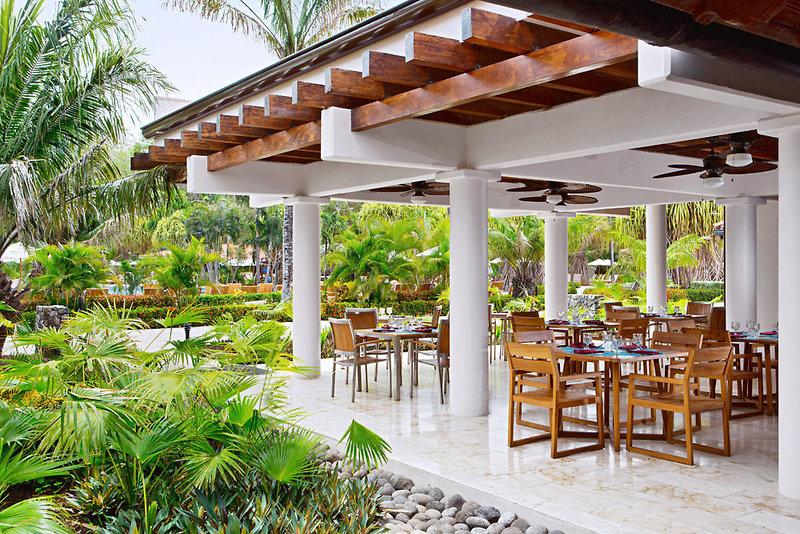 Außenterrasse des Westin Reserva Conchal, eines All-Inclusive Golf Resorts mit Holzmöbeln und Palmen