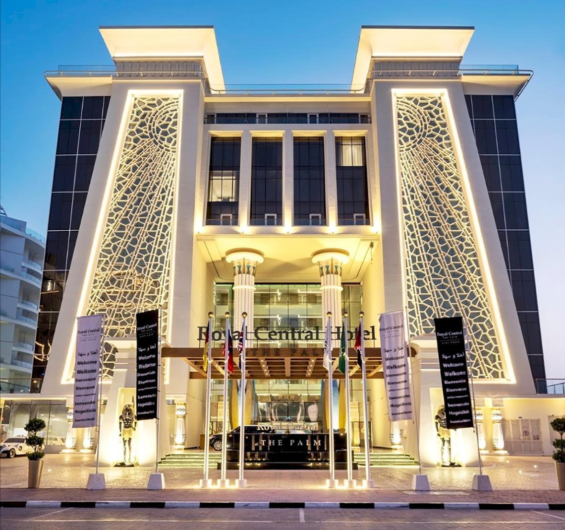 Eingangsbereich des Royal Central Hotel The Palm mit Beleuchtung und Willkommensschildern.