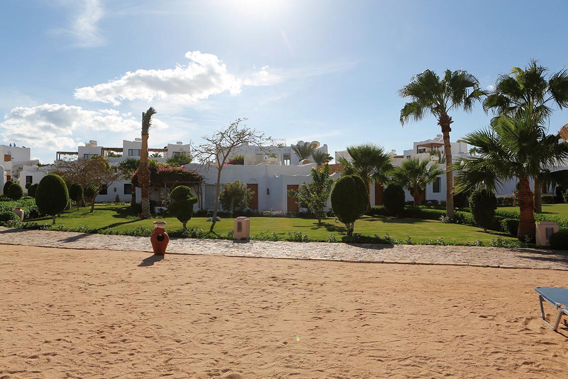 Außenansicht des Sharm Club Beach Resorts mit weißen Gebäuden und üppigem Garten