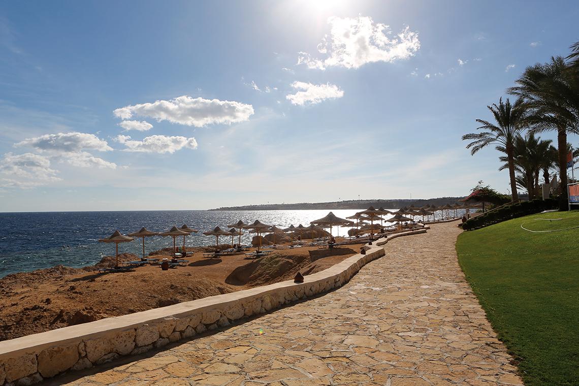 Strandweg des Sharm Club Beach Resort mit Sonnenschirmen und Blick auf das Meer.