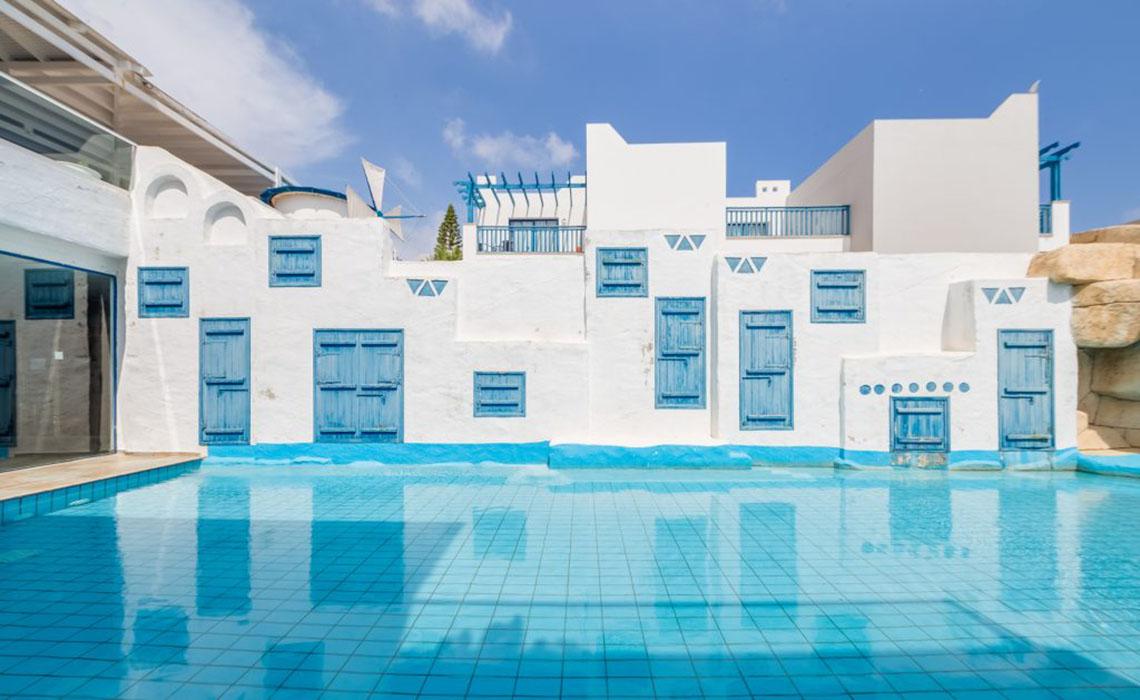 Außenbereich des Callisto Holiday Village mit blauen Fensterläden und einem großen Swimmingpool.