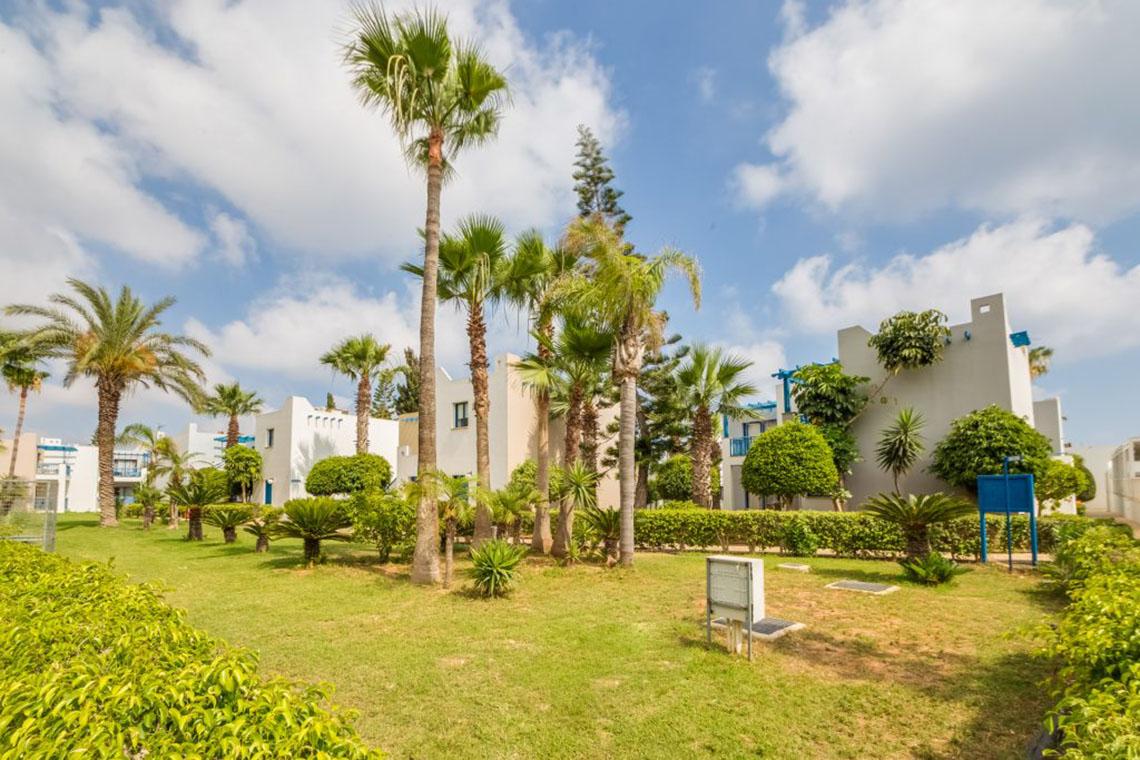 Außenbereich des Callisto Holiday Village mit weißen Gebäuden und grünen Palmen.