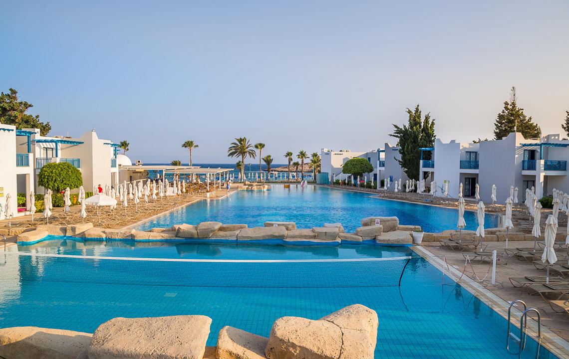 Großer Pool des Callisto Holiday Village mit umliegenden Umkleidekabinen und Liegestühlen.