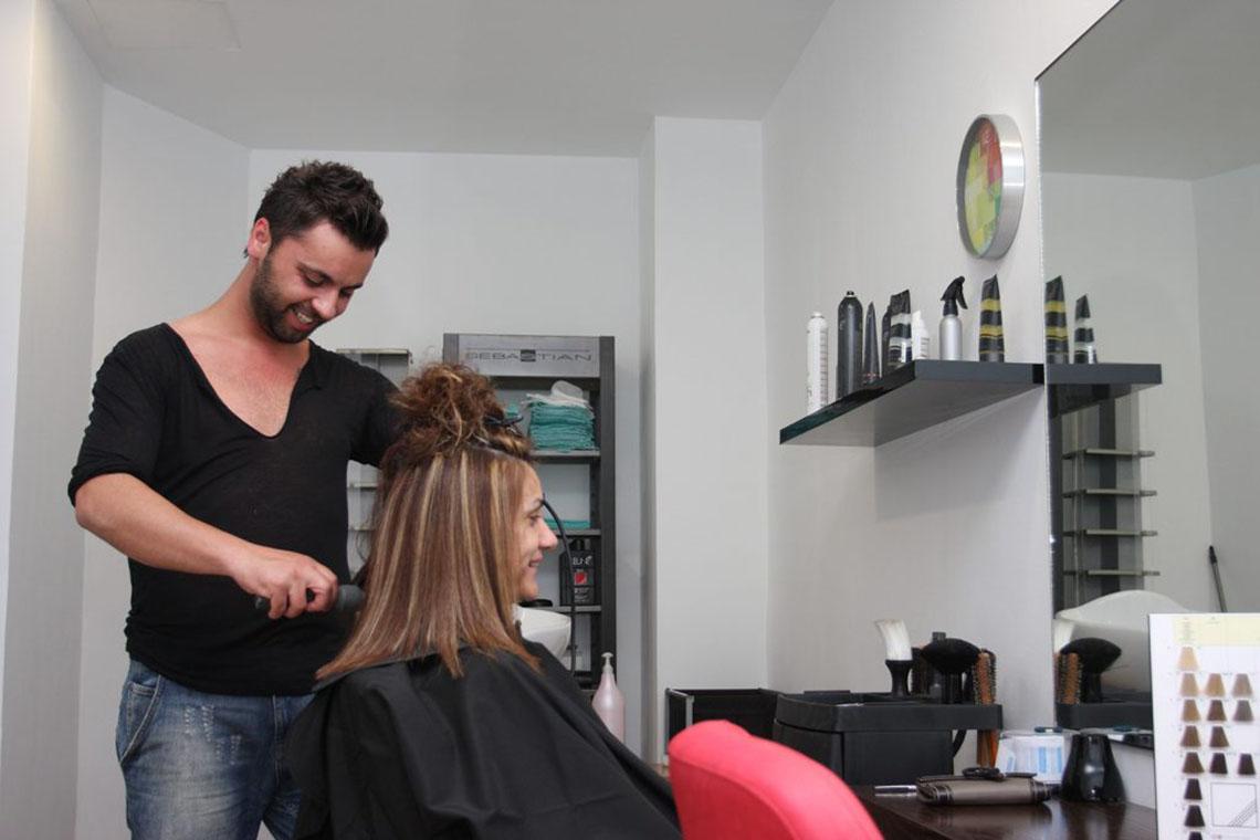 Ein Mann, der in einem Salon eine Kundin frisiert, während sie in einem roten Stuhl sitzt.