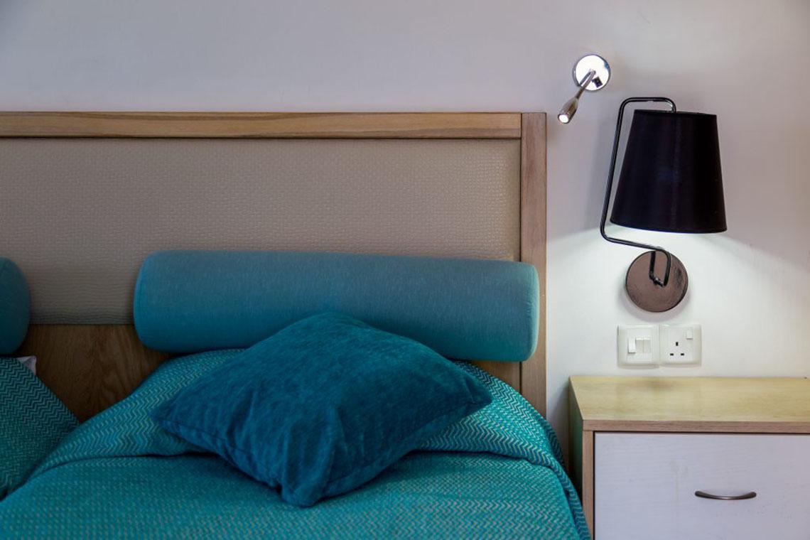 Ein Bett mit blauen Kissen und einer Wandlampe im Schlafzimmer des Callisto Holiday Village.