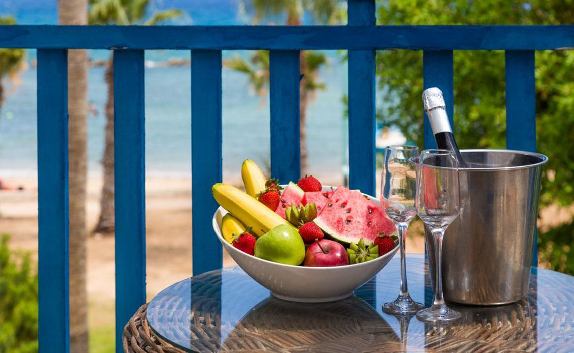 Ein Balkon des Callisto Holiday Village mit einer Obstschale, zwei Weingläsern und einer Flasche Champagner.